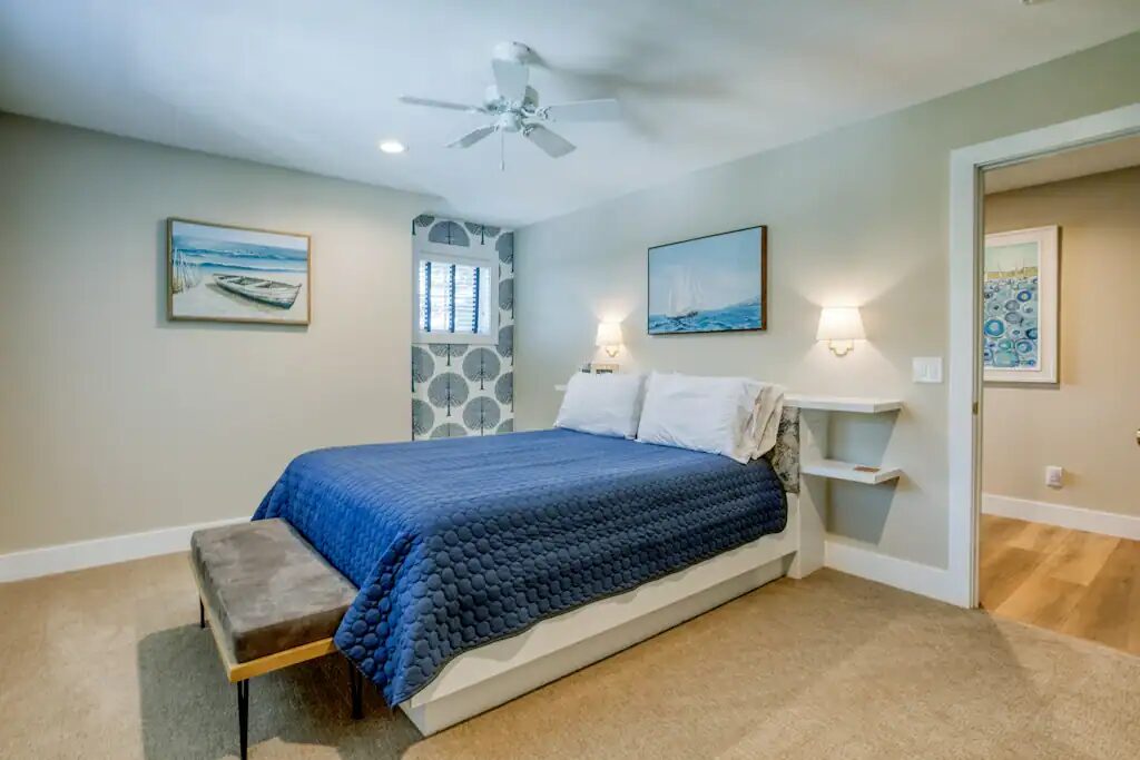 A second bedroom on the upper floor with a blue quilted bed, bedside sconces and framed lake prints.