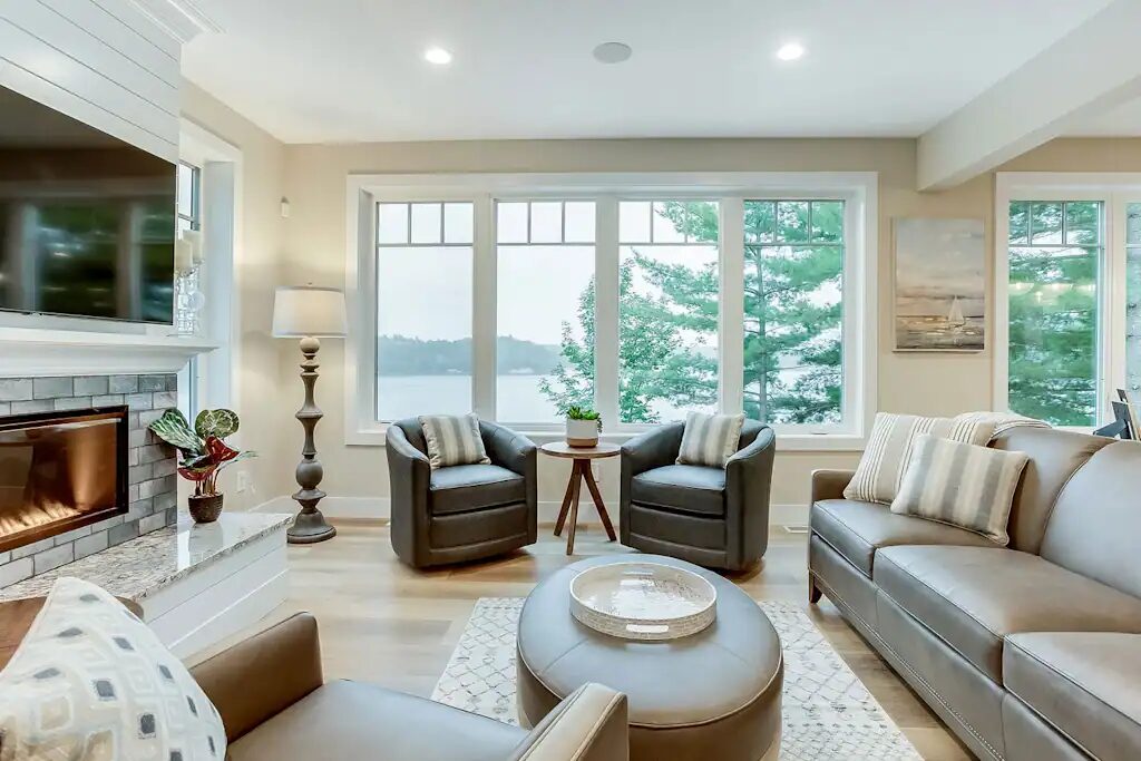 The main living room with a stone fireplace, armchairs and a sofa facing a wall of windows onto the lake.