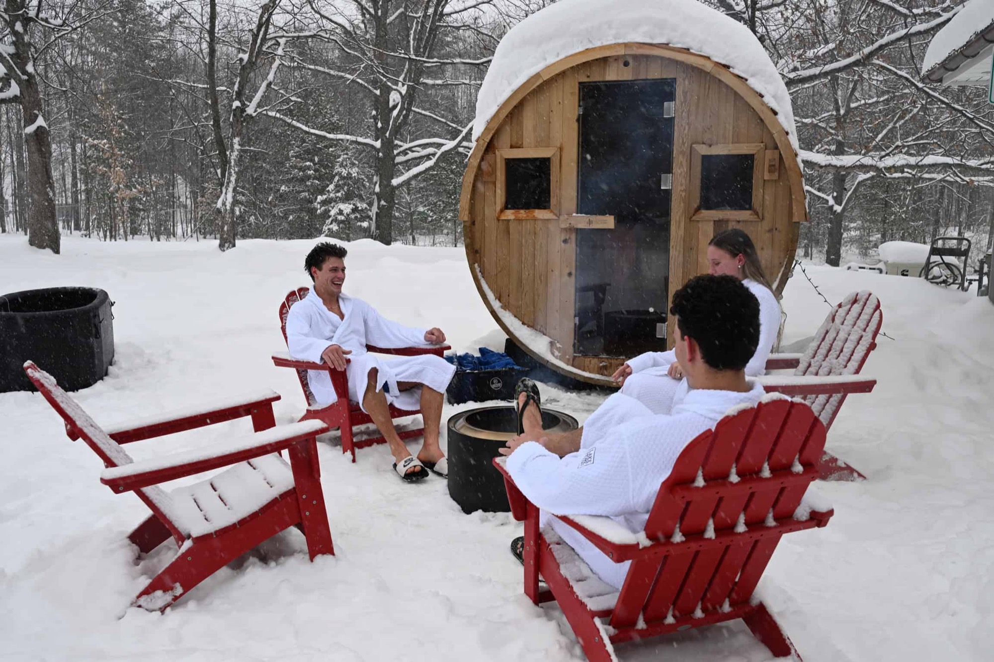 Snow-covered chairs and a barrel sauna outside a Lakemore house in winter.