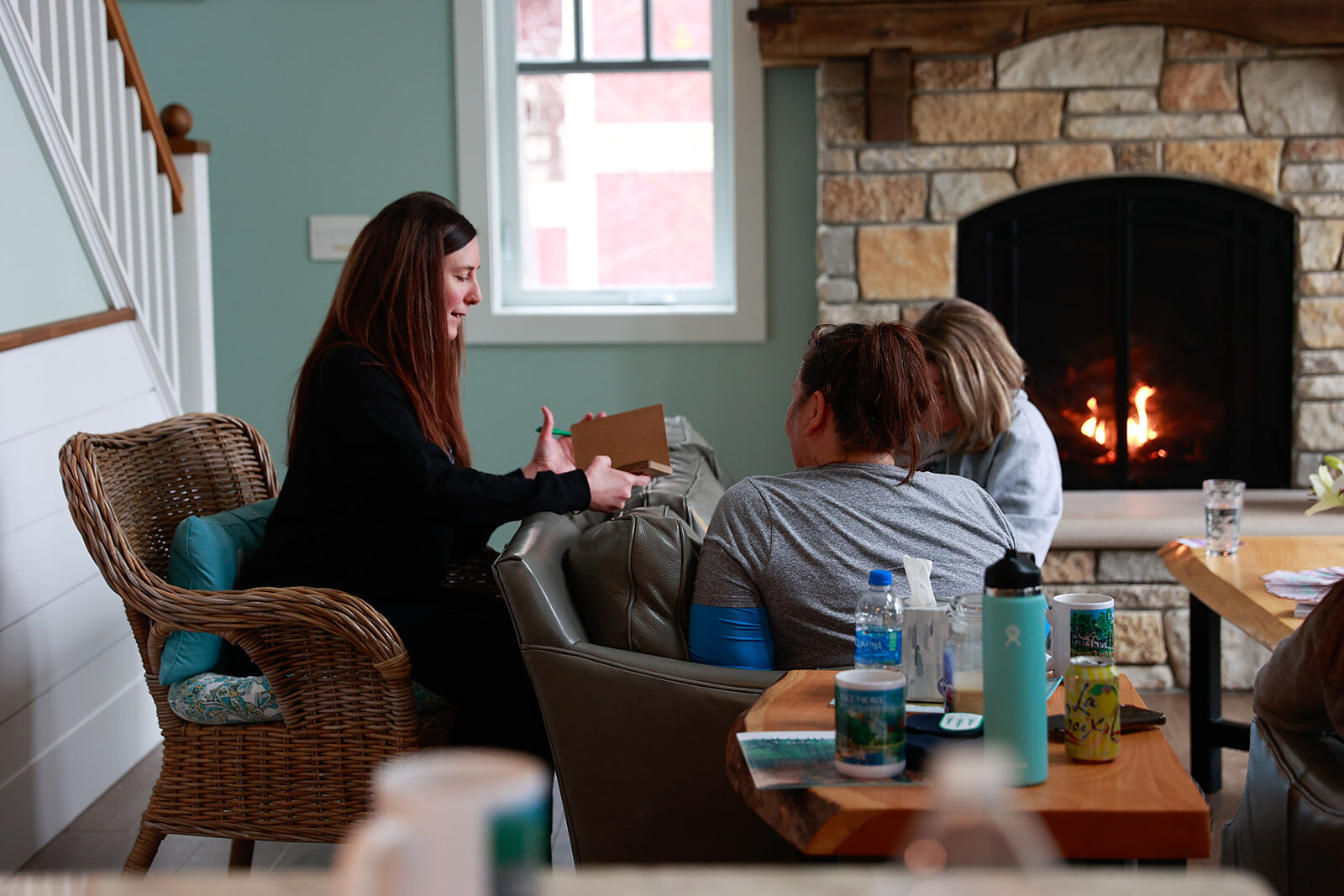 A group of women sitting in armchairs around a lit fire, notebooks open on their laps.